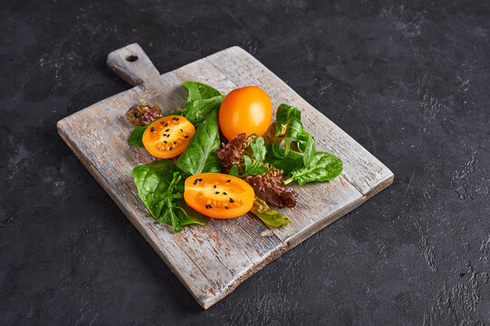 Ingredients for dieting salad - tomatoes, arugula, spinach, lettuce on wooden cutting board on dark background, selective focus, cloce up