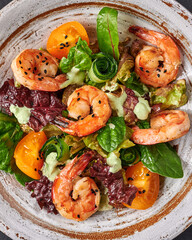 Food backgrownd salad with fried shrimp, yellow tomatoes, arugula, spinach, lettuce and sauce on a ceramic plate, vertical orientation, copy space