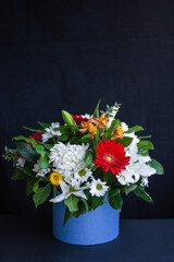 Bright bouquet of gerberas, chrysanthemums, lilies, green leaves in a gift box on a dark background. Selective focus.