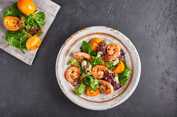 Fototapeta na wymiar Homemade salad with fried shrimp, yellow tomatoes, arugula, spinach, lettuce and sauce on a ceramic plate and ingredients on the cutting board, top view, copy space