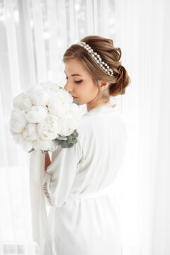beautiful bride with a white robe is going at home. fees of the bride. wedding day of the newlyweds. a hoop on the bride's head. decoration on the girl's head. wedding bouquet of flowers.