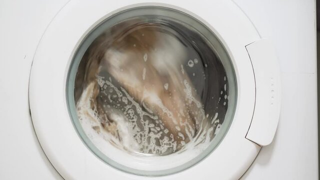 White washing machine washes dirty color clothes. Washing clothing in domestic washing machine in home. Close-up video of spinning drum washing machine