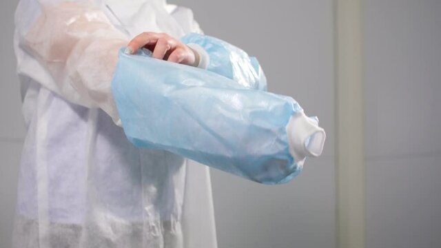 Nurse in disposable protective suit puts on blue oversleeves