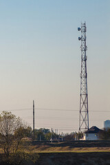 Cell tower on the outskirts of the city against the background of dirty blue sky and wires