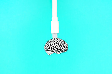 White data cable attached to a small steel copy of a human brain isolated on a blue background. Creative education and knowledge transfer concept.