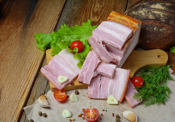 Smoked sliced pork belly, bacon, ham with herbs, tomatoes and black pepper on food paper. Wooden rustic background.Selective focus.