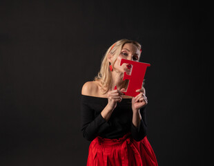 A girl holds the letters of the word LOVE valentine, a Valentine's day board, wedding hearts on the floor. the formula for the occasion. festive, frame in red dress girl, barefoot