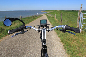 a coastal landscape in zeeland, holland with a bicycle handlebar at a dike crossing of the seawall along the westerschelde sea in summer and a cargo ship in the water with high tide