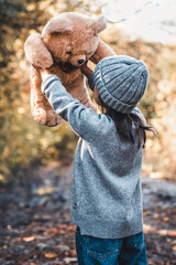 Little girl holds a bear in her arms on the background of nature on an autumn day.