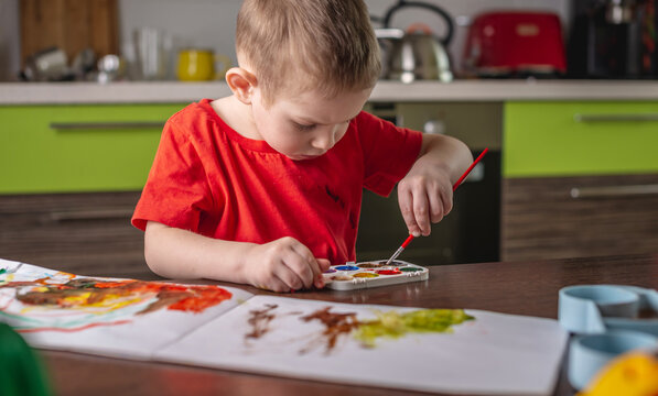 Child in a red T-shirt paints with colorful watercolors at the table
