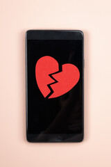 Smartphone with broken red paper heart on it. Parting, unrequited love concept,