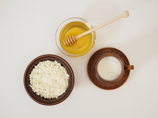 Healthy tasty breakfast in earthenware on a white background. Natural farm dairy products milk, cottage cheese and fresh honey. Flat lay, top view