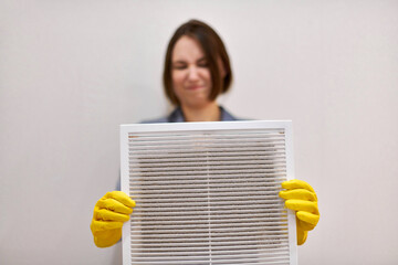 Woman holding dirty and dusty ventilation grille, disgusted