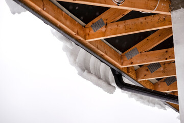 The roof of a single-family house is covered with snow, visible roof trusses from the bottom and a hanging cap of snow on the gutter.