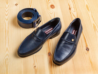 Shoes and a trouser belt made of dark blue leather against a background of light boards