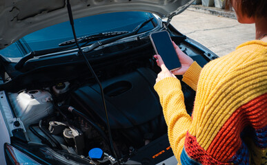 A woman standing in front of a car with a bonnet Overlooking the engine room And is using the phone to contact the auto repair center Via smartphone app