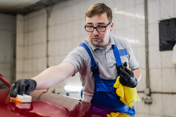 Car detailing - Man applies nano protective coating or wax on red car. Covering car bonnet with a liquid glass polish.