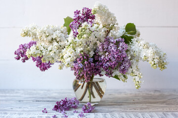 White lilac and purple lilac in glass vase on wooden table. Spring branches of blooming lilac festive bouquet of flowers.