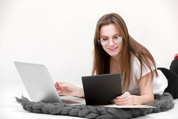 Naklejka premium A smiling young girl in glasses sits with a laptop. Education, remote work and blogging. Isolated on a white background.