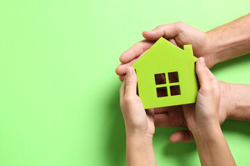 Couple holding house model on light green background, top view. Space for text
