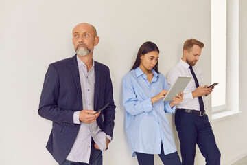 Bored, serious multi-aged people lining up in office waiting area and using gadgets