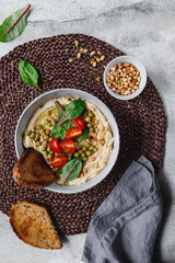 Hummus with green pea, pine nuts, tomatoes and swiss chard. Vegetarian healthy dish, top view.
