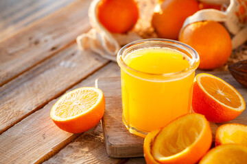 Glass of freshly sqeezed orange juice on a wooden table. Natural source of vitamins, healthy beverage for ideal breakfast. Bright sunny summer day. Close up, copy space for text.