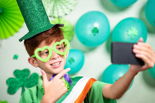Young kid on video call during saint patricks day celebration on mobile phone and showing decorated background over video call - concept of distant festivels due to coronavirus or covid-19 pandemic. - Powered by Adobe