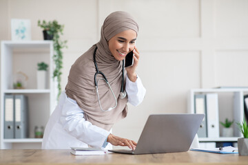 Busy female doctor talking on phone and checking her laptop