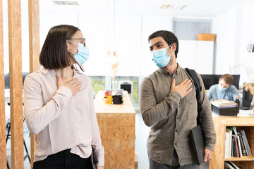 Hispanic coworkers greeting with the hand on chest. Working in the office during Coronavirus pandemic concept.