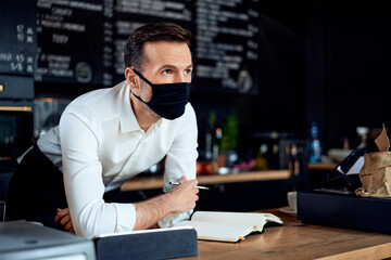 Portrait of worried cafe small business owner wearing mask behind the counter