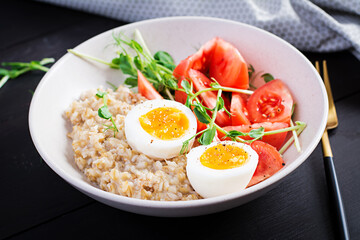 Breakfast oatmeal porridge with boiled egg, cherry tomatoes and microgreens. Healthy balanced food.