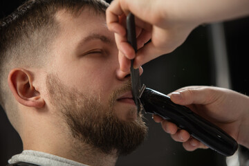 Close up of client of master barber, stylist during getting care and new look of mustache and beard. Professional occupation, male beauty and self-care concept. Soft colors and focus, vintage.