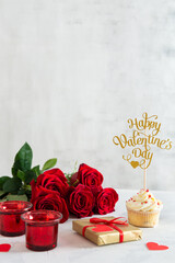 St. Valentine's Day background with product place or copy space. Cupcake with small hearts, gift and red roses on light concrete background. Romantic love background. Happy Valentines Day.