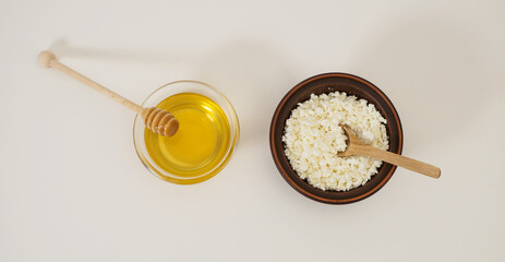 Banner with rustic fresh cottage cheese in handmade earthenware bowl, wooden spoon, natural wholesome honey, honey ladle on white background. Healthy tasty ecological breakfast in crockery. Dairy