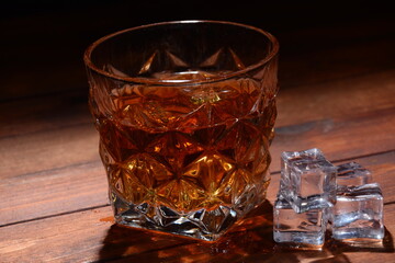 Glass of whisky or whiskey or bourbon on ice  on wood bar