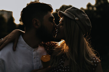 Man and woman kiss on date in park during sunset. Portrait of romantic couple embracing in evening