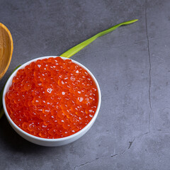 Red caviar in a wooden cup on a grey background with a spoon.