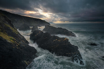 Stormy seascape sunset scene with black rocks