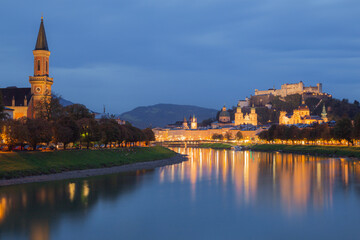 Evening old town cityscape view along the Salzach River in Salzburg, Austria of Protestant parish Salzburg Christ Church and the Pfarre Mulln Church and the hilltop Fortress Hohensalzburg.