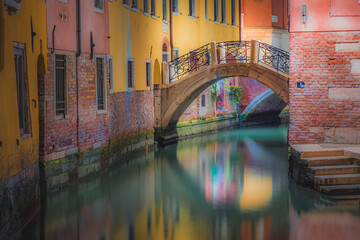 Fototapeta na wymiar Bright, colourful Venetian architecture with a bridge over a calm canal during a quiet night in a secluded residential area of old town Venice, Italy.