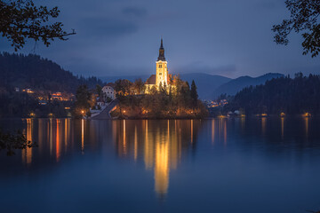 Fototapeta na wymiar Evening twilight view of Pilgrimage Church of the Assumption of Maria lit up at Lake Bled, Slovenia in the Julian Alps.