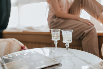 Photo of two crystal glasses with champagne and magazine on marble table against background of...