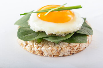 Puffed exploded wheat grains with fried egg and spinach leaves on a light wooden background. Close-up