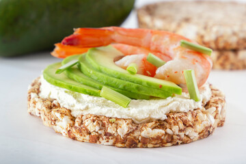 Puffed exploded wheat grains with shrimps and avocado slices on a thin layer of soft cheese on a light wooden table. Close-up