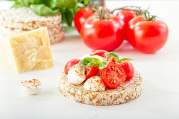 Puffed exploded wheat grains with slices of mozzarella and chili tomato sprinkled with pepper on a light wooden table against the background of a head of cheese. tomatoes and herbs. Close-up