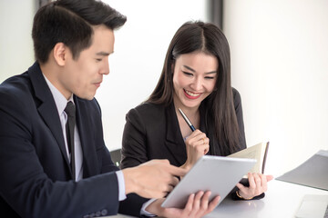 Asian businessman and businesswoman meeting to learn about new job using concept tablet and taking notes at the office.