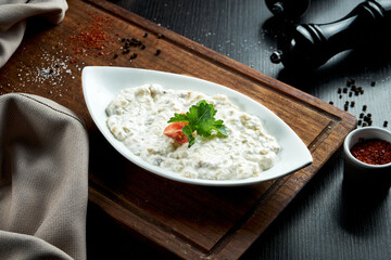 Traditional Arabian eggplant dish Baba Ghanoush with olive oil and herbs in white yogurt. Wood table. Close up