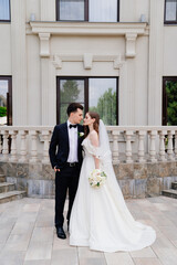 Naklejka premium beautiful newlyweds stand against the background of a light building. 