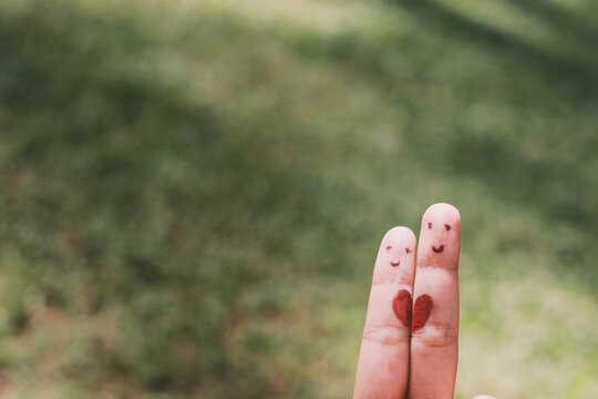 Red heart shape on two fingers with face image while smiling face with nature bokeh background. copy space. Happy couple in love.